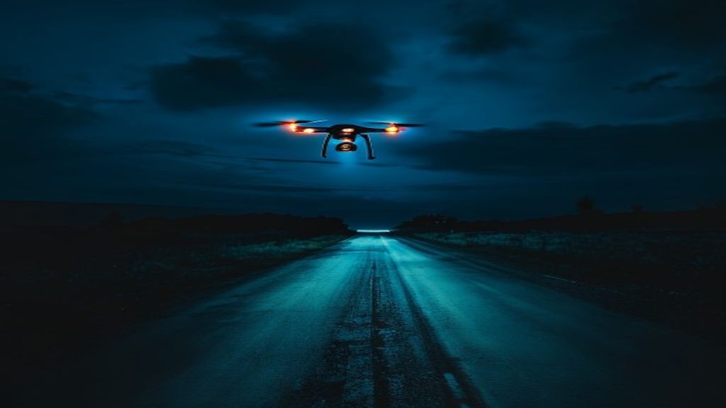 Drone with cyan and amber LED lights flying at night over a dark road
