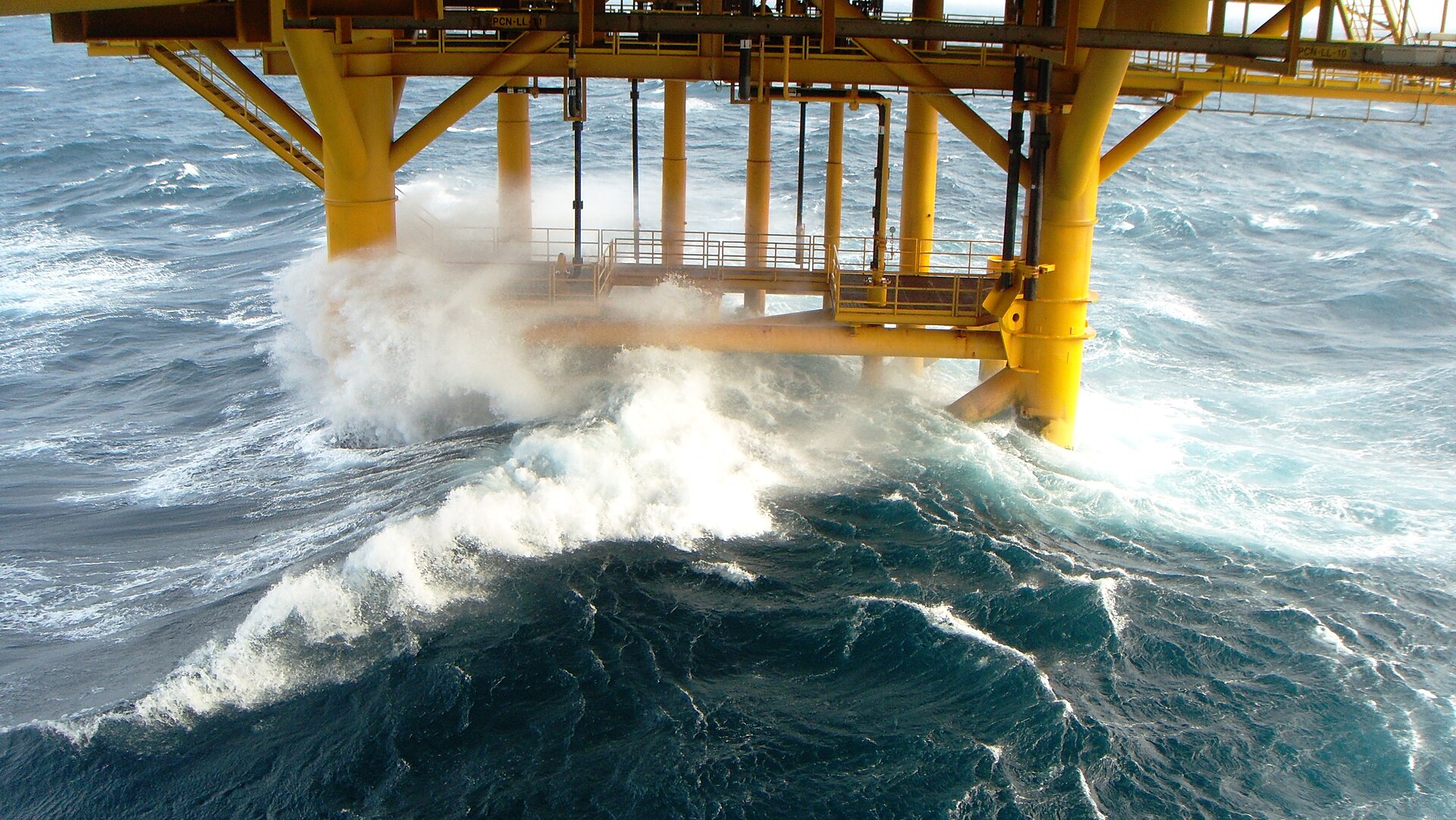 Yellow offshore oil platform jacket legs in a breaking wave at the splash zone
